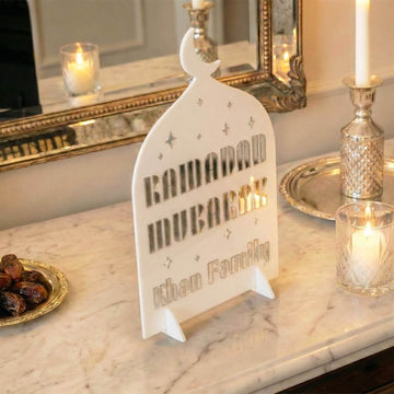 Schräge Nahansicht des weißen Aufstellers Familienname (Modern) mit silberner Schrift und Kerze