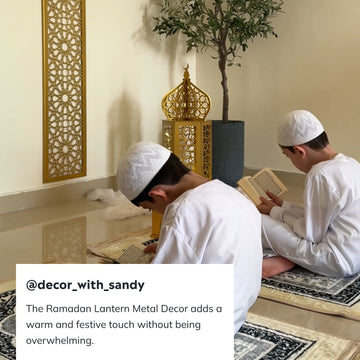 Two boys reading beside a gold Ramadan lantern and a laser-cut wall panel in a prayer corner