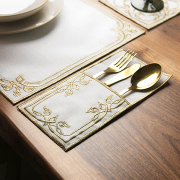 Gold interlocking scroll cutlery pouch holding a gold fork, knife and spoon beside the placemat corner