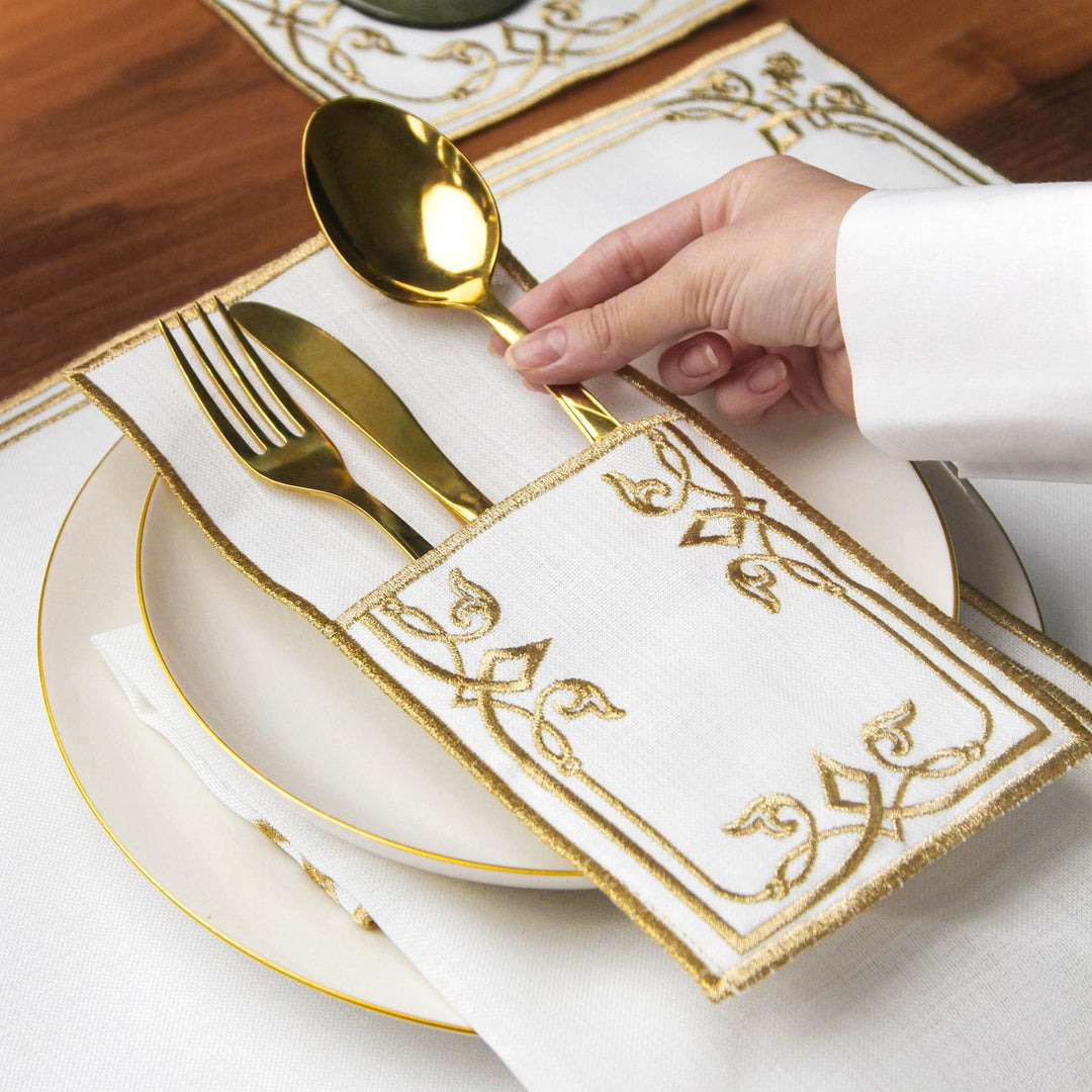 Hand placing a gold spoon into the Gold interlocking scroll cutlery pouch on a plate