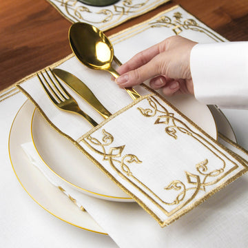 Hand placing a gold spoon into the Gold interlocking scroll cutlery pouch on a plate