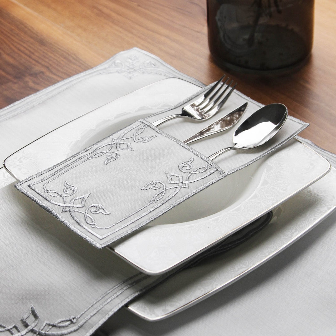 Silver interlocking scroll cutlery pouch resting on a square plate with silver cutlery