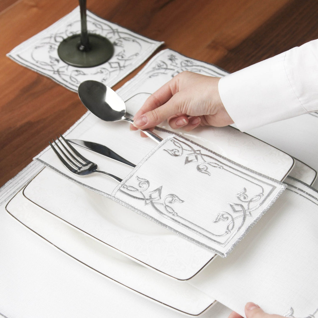 Hand placing a silver spoon into the Silver interlocking scroll cutlery pouch on a plate