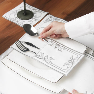 Hand placing a silver spoon into the Silver interlocking scroll cutlery pouch on a plate