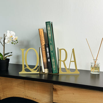 Gold IQRA Latin letter bookends with books, wide view with an orchid and reed diffuser
