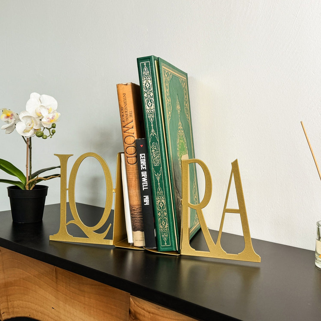 Gold IQRA Latin letter bookends holding a green Quran and books, angled view on a black cabinet