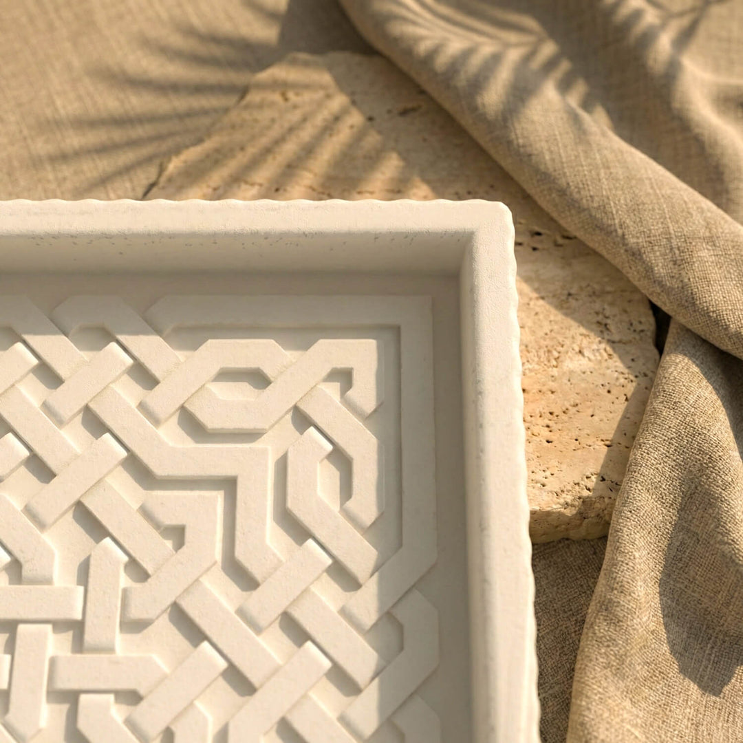 Decorative stone tray with geometric pattern next to a textured beige fabric
