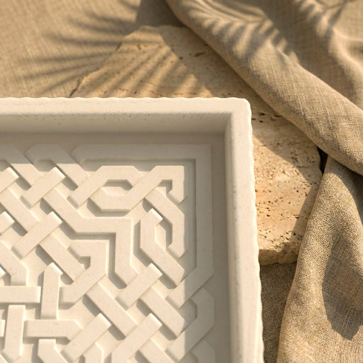 Decorative stone tray with geometric pattern next to a textured beige fabric