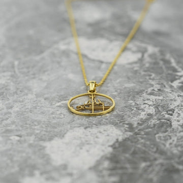 Gold Allahu Akbar pendant lying at an angle on marble, with the chain trailing upward