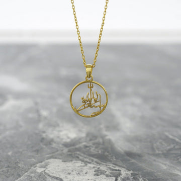Gold Astaghfirullah Islamic necklace with a round pendant hanging on a gray marble surface