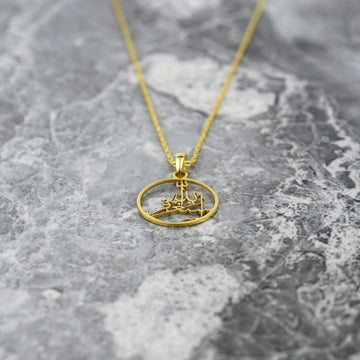 Gold Astaghfirullah pendant lying low on marble with the chain trailing upward