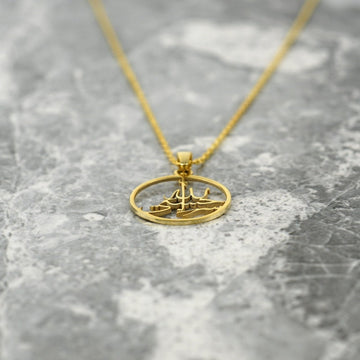 Gold Hasbiyallah pendant lying low on marble with the chain trailing upward