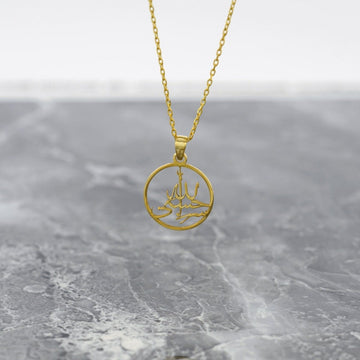Gold Hasbiyallah Islamic necklace with a round pendant hanging on a gray marble surface