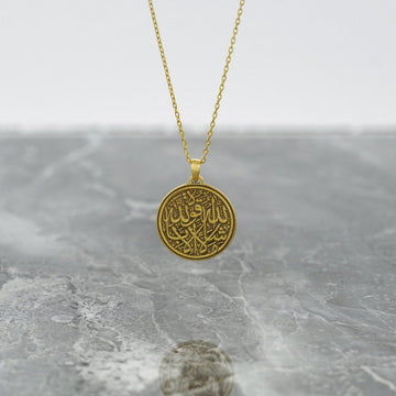 Collier islamique doré Mashallah La Quwwata Illa Billah avec un pendentif disque rond sur du marbre