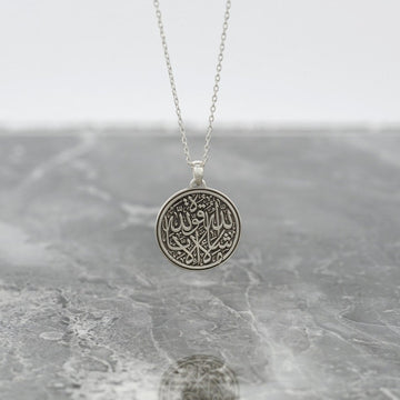 Collier islamique argenté Mashallah La Quwwata Illa Billah avec un pendentif disque rond sur du marbre