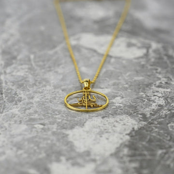 Gold Subhanallah pendant lying low on marble with the chain trailing upward