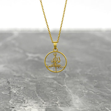 Gold Subhanallah Islamic necklace with a round calligraphy pendant hanging on a gray marble surface