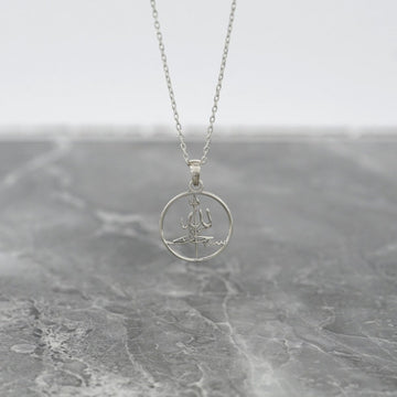 Silver Subhanallah Islamic necklace with a round pendant hanging above gray marble