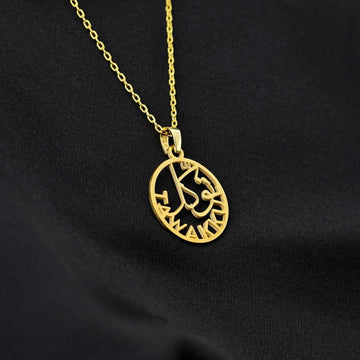 Gold Tawakkul pendant tilted on its chain, draped over black fabric
