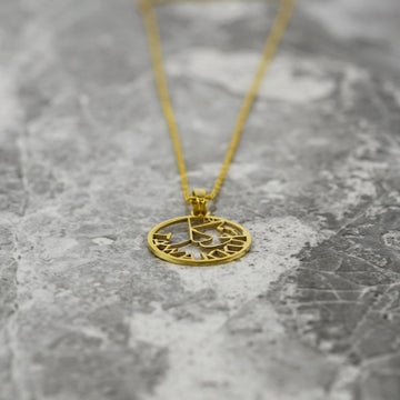 Gold Tawakkul pendant lying low on marble with the chain trailing upward