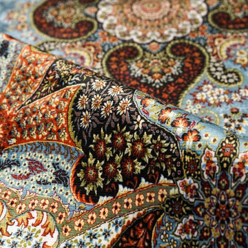 Gros plan du tapis de prière floral bleu et beige roulé, montrant des détails floraux rouges et orange