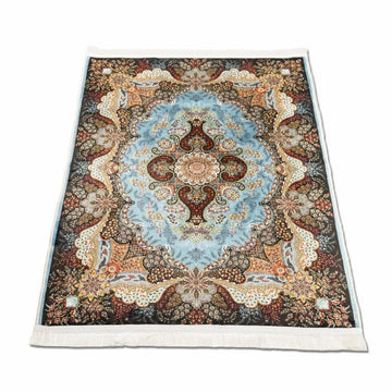 Tapis de prière à motifs floraux bleu et beige déplié en biais avec franges blanches sur fond blanc