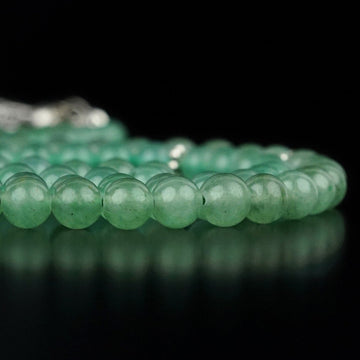 Side view of green aventurine quartz prayer beads in a row with a reflection on black