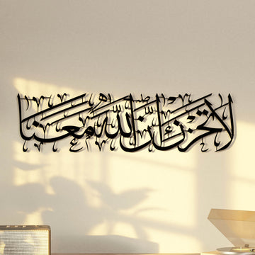 لوحة جدارية معدنية لسورة التوبة الآية 40 باللون الأسود، منظر أمامي لخط «لا تحزن إن الله معنا»