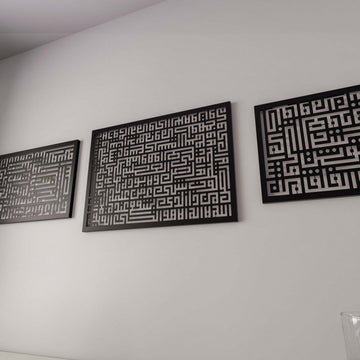 منظر جانبي قريب للوحتي آية الكرسي والسورتين السوداوين بالخط الكوفي على جدار رمادي