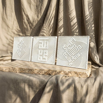 Ensemble de trois carreaux coufiques en relief de pierre blanche alignés sur une dalle, vue depuis la gauche