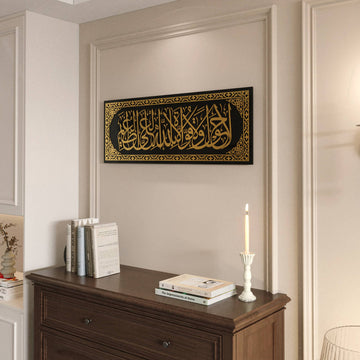 Gold acrylic La hawla wa la quwwata illa billah glass wall art on a paneled wall beside a dresser