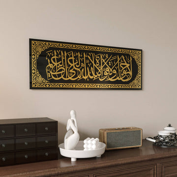 Gold acrylic La hawla wa la quwwata illa billah glass wall art on black glass with a gold border, above a dresser