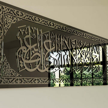 Close-up of silver acrylic calligraphy and border pattern on the black glass wall art, reflecting a window