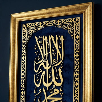 لقطة مقربة بزاوية للإطار الخشبي المطلي بالذهبي وخط كلمة التوحيد الأولى الذهبي على مخمل أزرق