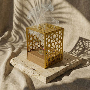 Wooden base mabkhara with a gold Star Lattice metal frame, incense smoke rising, on a stone slab