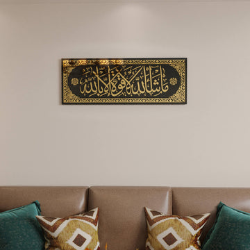 لوحة زجاج مقسّى «ما شاء الله لا قوة إلا بالله» بأكريليك ذهبي على جدار خالٍ فوق ظهر أريكة، لقطة مقربة