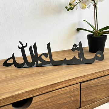 ديكور طاولة معدني أسود «ما شاء الله» على مكتب خشبي بجانب زهرة أوركيد