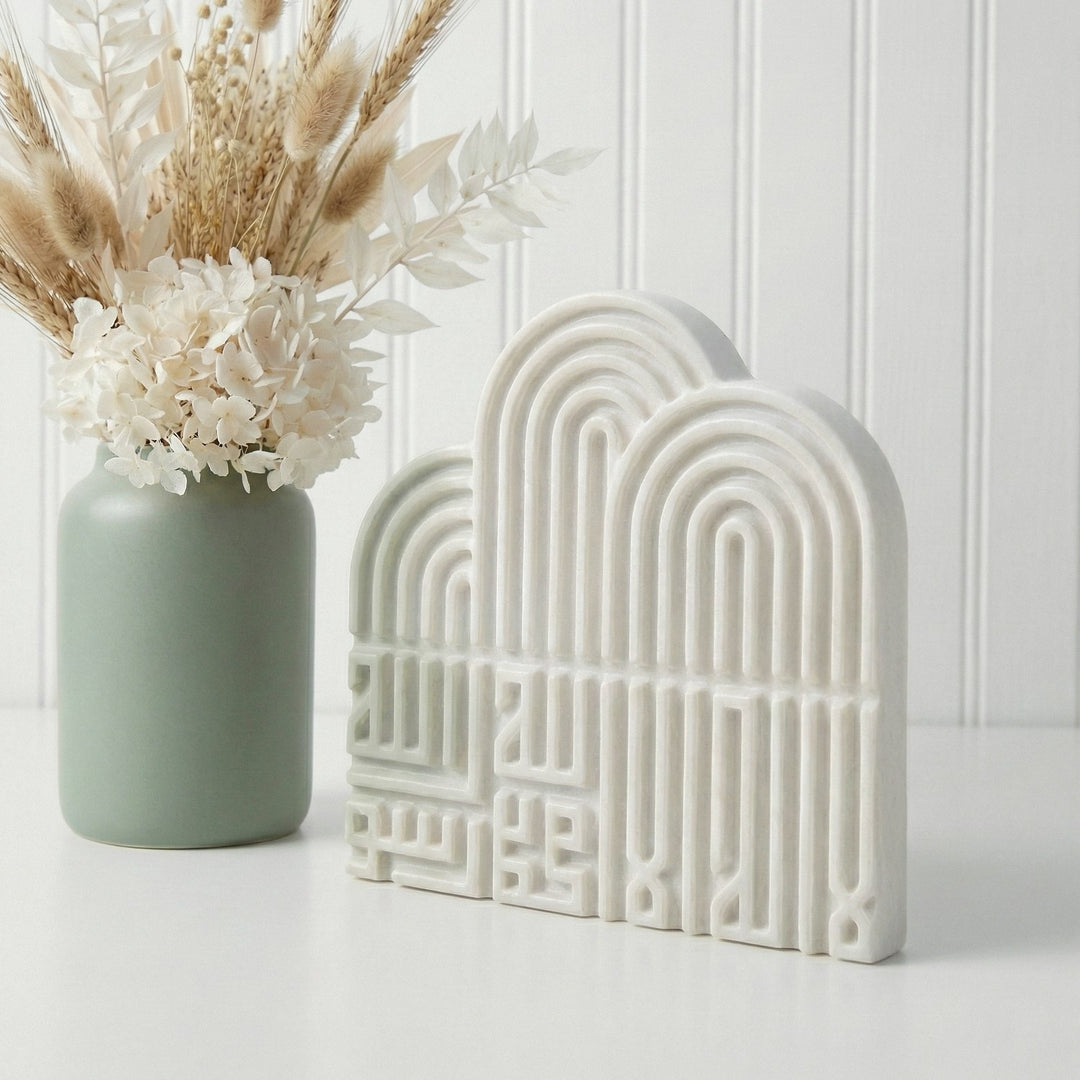 Decorative arch-shaped ceramic piece next to a vase with flowers on a white surface.