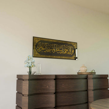Gold Surah Baqarah 144 mihrab verse glass wall art, distant view above a wooden chest of drawers