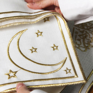 Gros plan du croissant et des étoiles brodés or sur la serviette tenue entre des mains