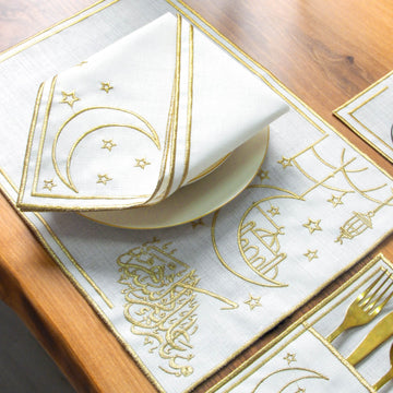 Serviette brodée or avec croissant et étoiles sur une assiette, à côté du set de table calligraphié