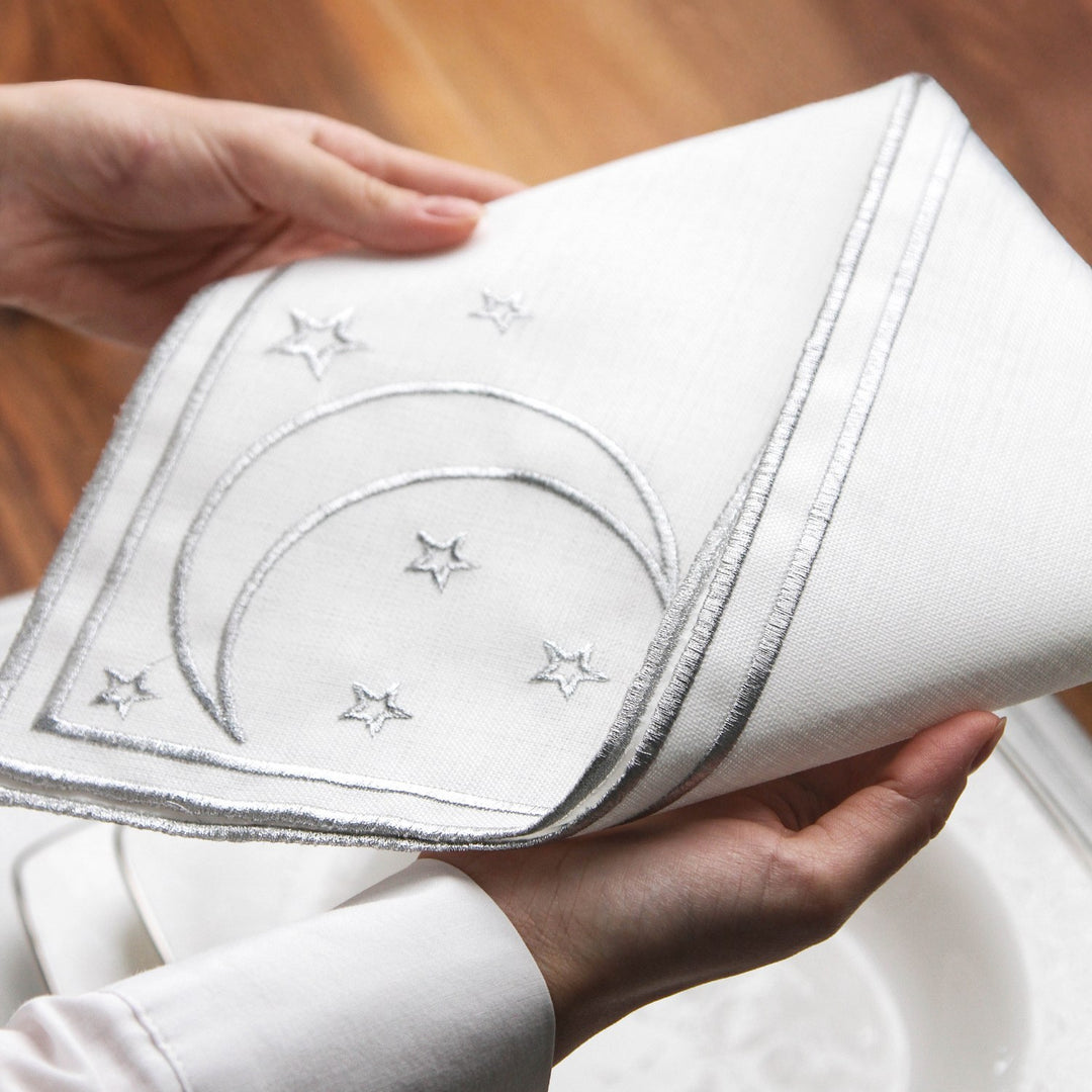 Mains soulevant au-dessus d'une assiette la serviette argentée brodée d'un croissant et d'étoiles