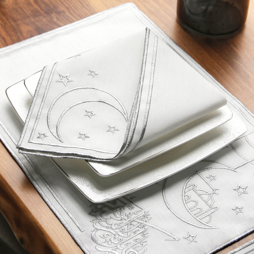 Serviette brodée d'un croissant et d'étoiles argentés sur assiettes carrées empilées, sur le set calligraphié argenté