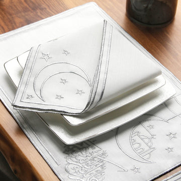 Serviette brodée d'un croissant et d'étoiles argentés sur assiettes carrées empilées, sur le set calligraphié argenté