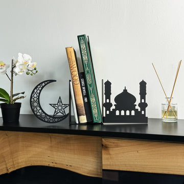 Schwarze Metall-Buchstützen in Moschee- und Halbmondform aus der Ferne auf einer Konsole mit kleiner Orchidee und Diffusor