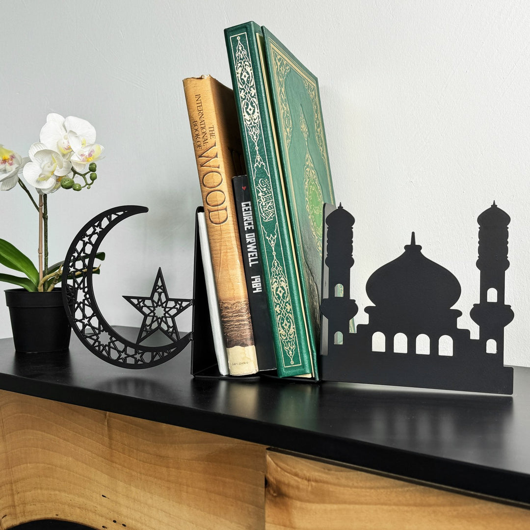 Schwarze Metall-Buchstützen in Halbmond- und Moscheeform flankieren einen grünen Koran und Bücher neben einer Orchidee
