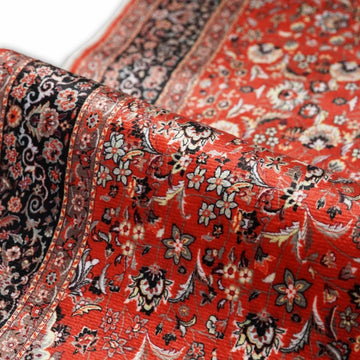 Gros plan sur le tapis de prière à fleurs rouge et noir plié pour montrer les poils et la bordure noire