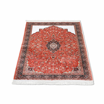 Tapis de prière musulman à fleurs classiques rouge et noir posé à plat et vu en angle sur fond blanc
