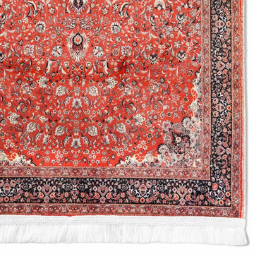 Coin du tapis de prière rouge et noir montrant le champ de fleurs dense, la bordure et les franges blanches