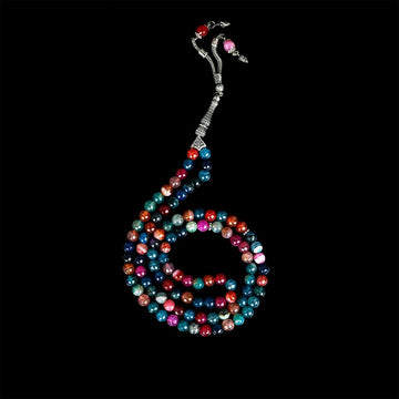 Multi-colored agate tasbeeh hanging in a long spiral from a silver tassel on black